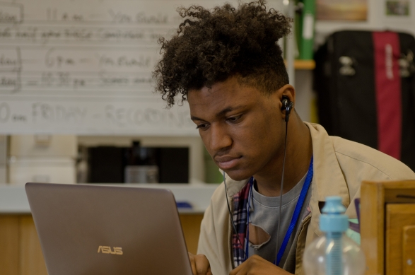 A young black man with earphones on his laptop
