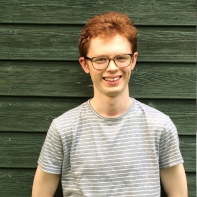Nicholas is a slender white man with ginger hair wearing glasses and a striped grey t-shirt