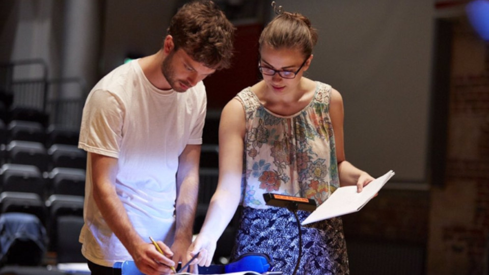 Two people stand over a table, annotating something with a pen