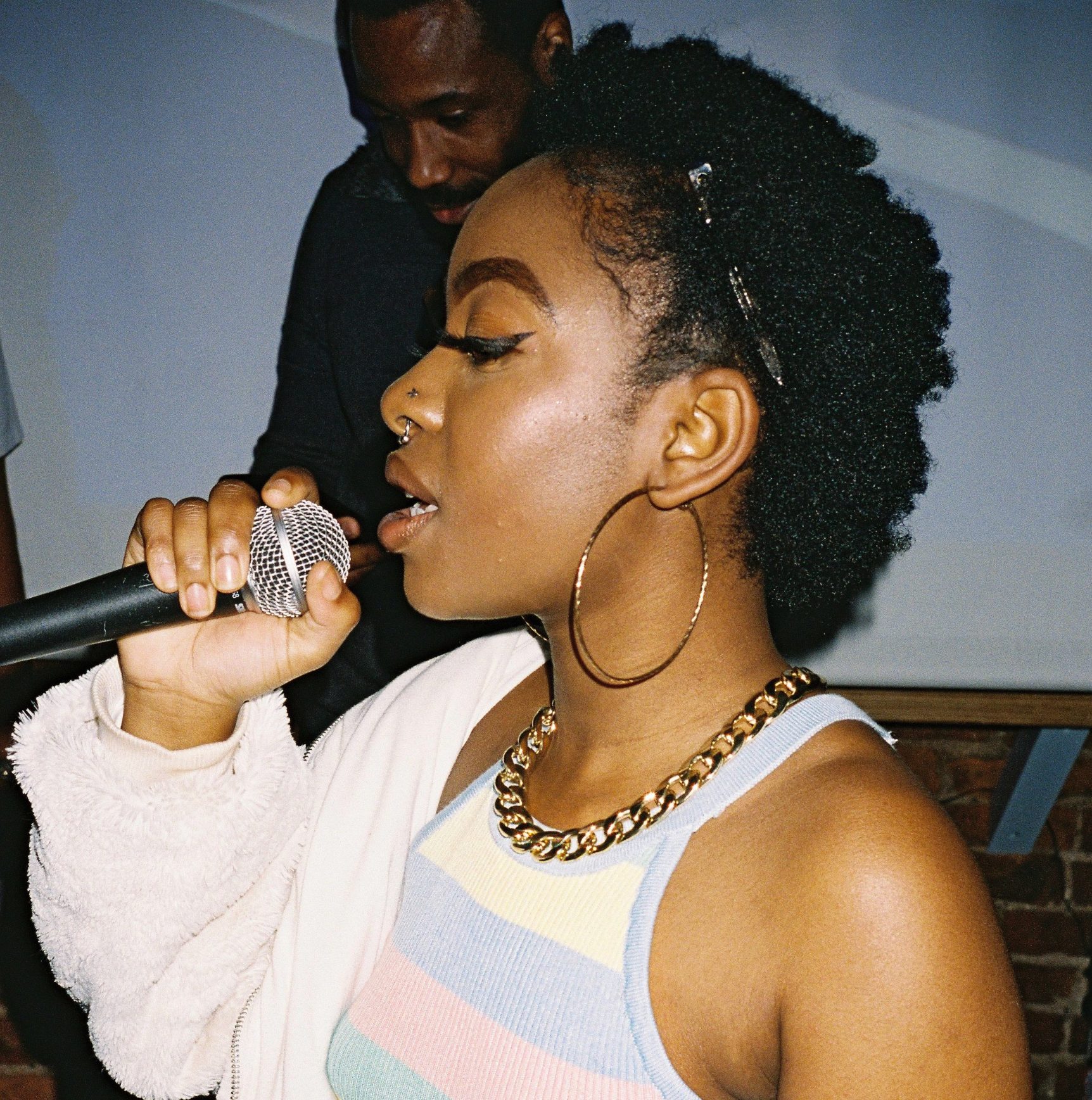 Rapper Medulla performs wearing pastel colours with a microphone close to her mouth and a DJ mixes in the background.