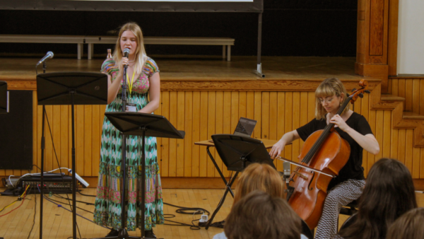 a photograph of a young person singing and performing alongside a musician playing the cello